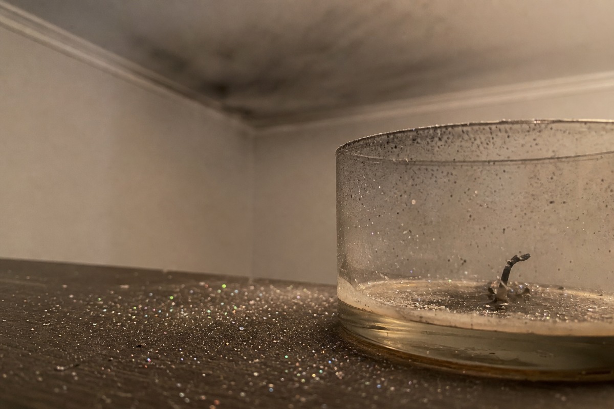 Pequenos brilhantes espalhados pela mesa à volta de uma vela já consumida, ao fundo uma fina película cinzenta de fuligem no teto.