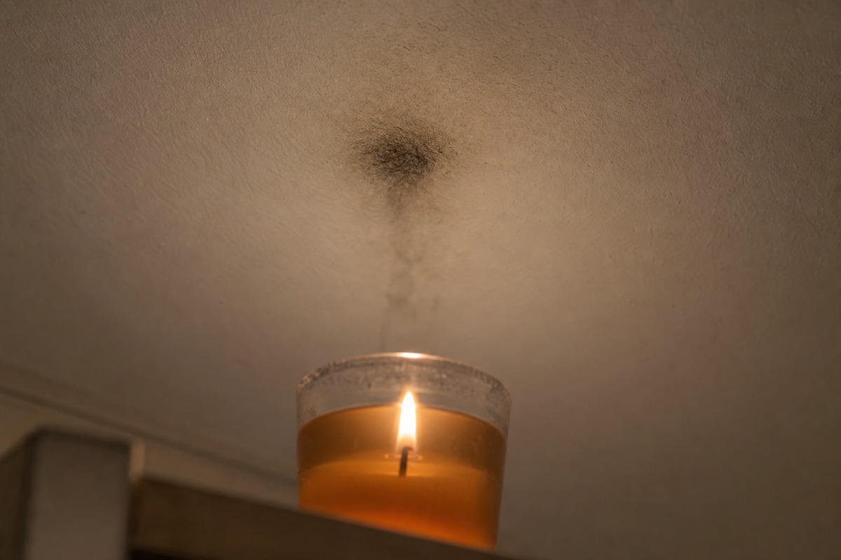 Mancha escura de fuligem no teto branco, mesmo por cima de uma vela de gel acesa num copo de vidro